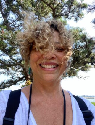 Denise Landis head shot, smiling with hair blowing in front of her face.