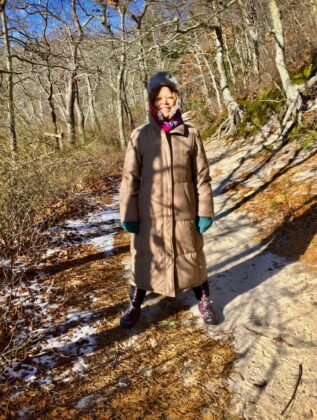 Denise Landis is heavy winter gear standing on a path with light snow on the ground.