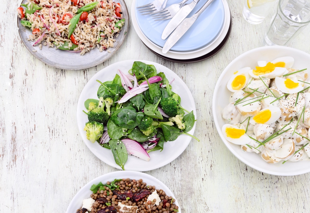 Overhead view of a variety assortment of side dishes, green salad, brown rice salad, lentil beetroot salad on a rustic background