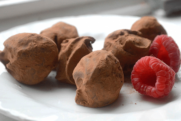 Chocolate truffles accompanied by fresh raspberries on a plate.