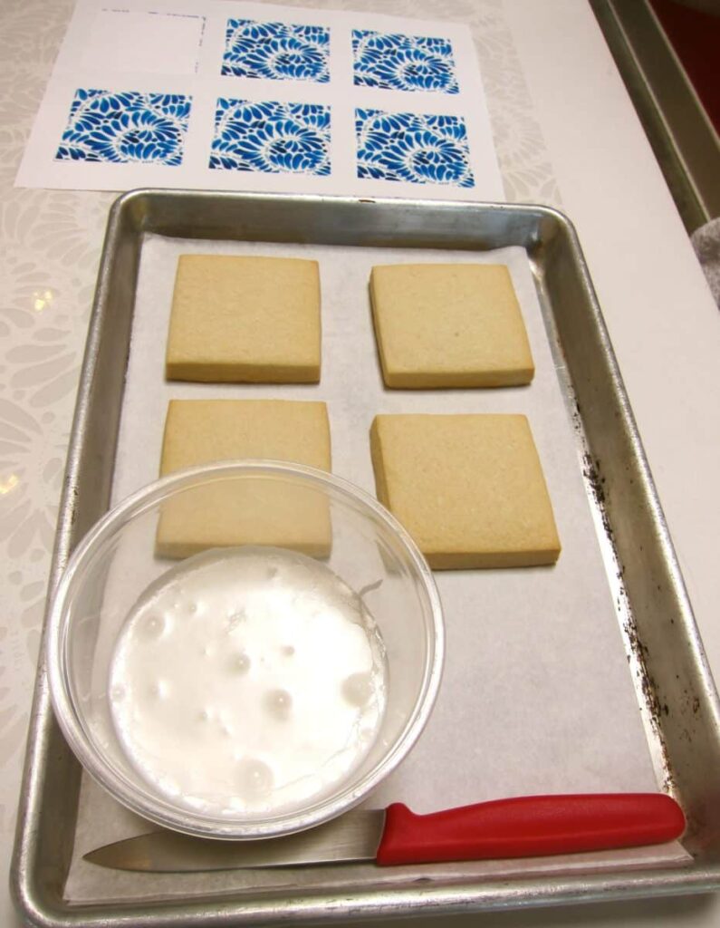 Plain rectangular cookies on a tray next to a bowl of white icing.