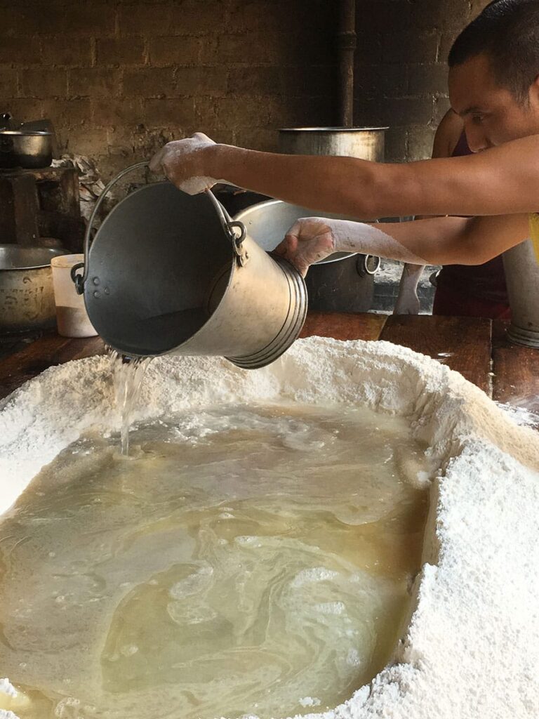 Hand pouring boiling water into a crater formed in a pile of flour.
