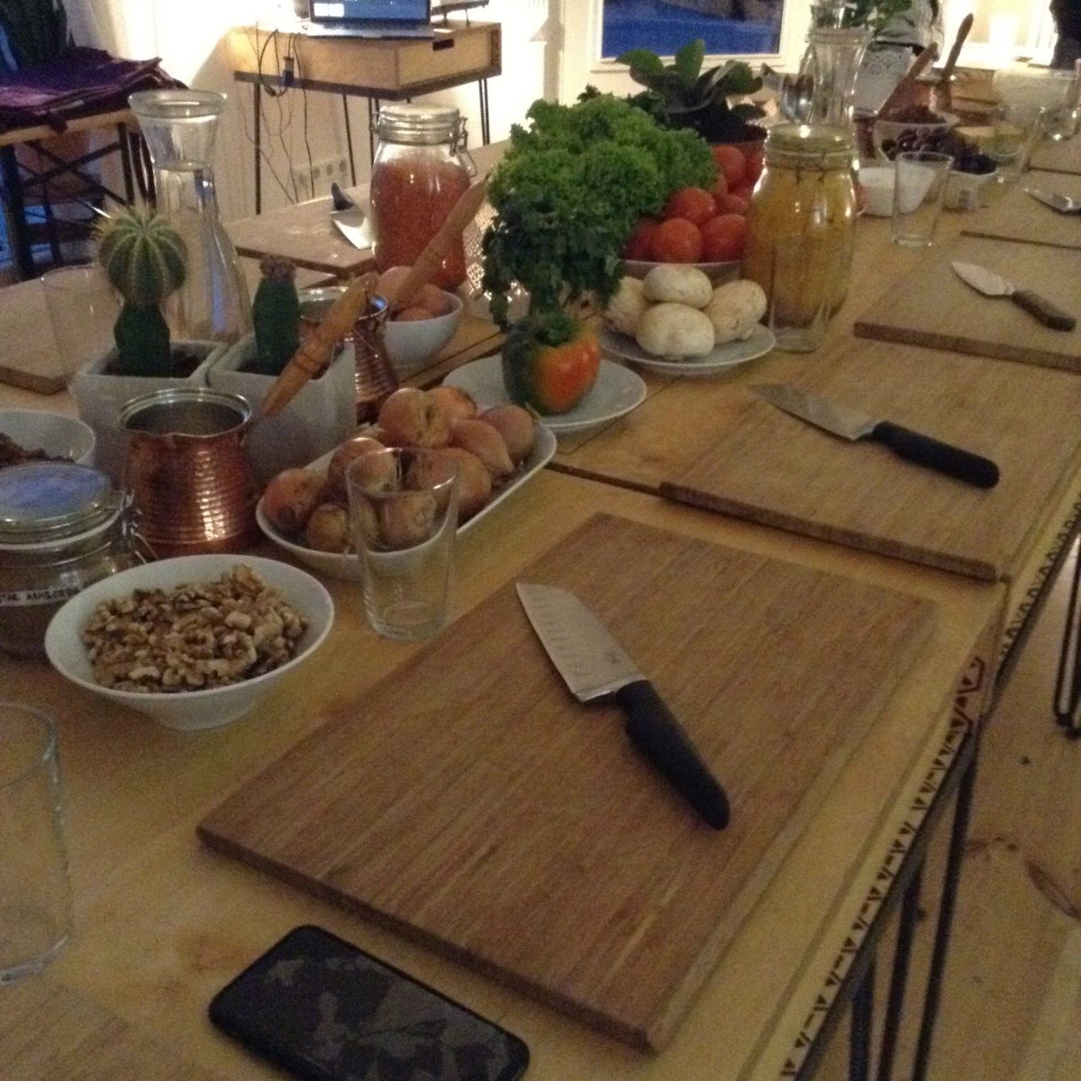 Table with several cutting boards and knifes, and food to prepare