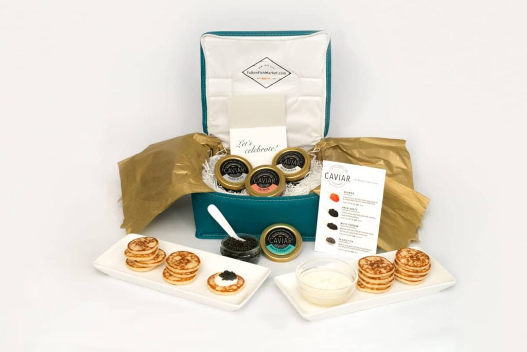 A luxurious caviar gift set displayed with blinis, creme fraiche, and an information card.