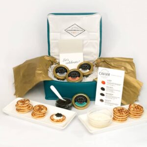 A luxurious caviar gift set displayed with blinis, creme fraiche, and an information card.
