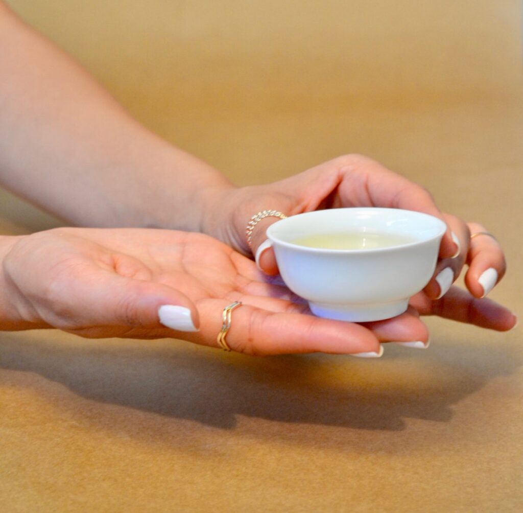 Hand presenting a cup of freshly brewed tea.