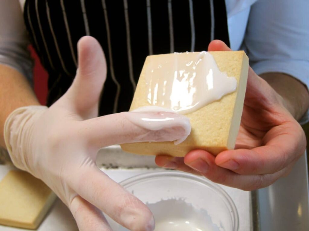 Hand applying white icing onto a rectangular cookie using a spatula.