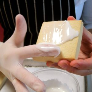 Hand applying white icing onto a rectangular cookie using a spatula.