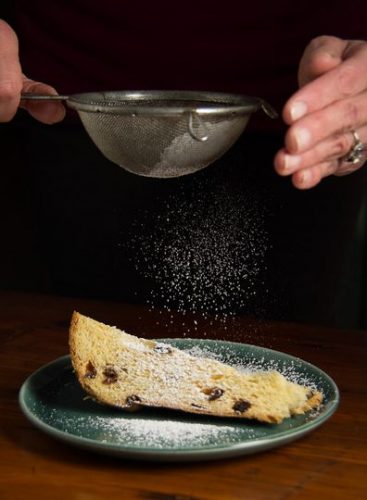 Confectioners' sugar being sifted over a slice of Italian fruit cake