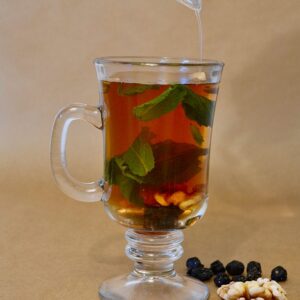 A cup of black tea with mint leaves, walnuts, cardamom, and raisins, presented on a wooden table.