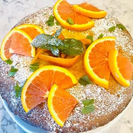 A top view of an orange olive oil cake garnished with orange slices and mint leaves.
