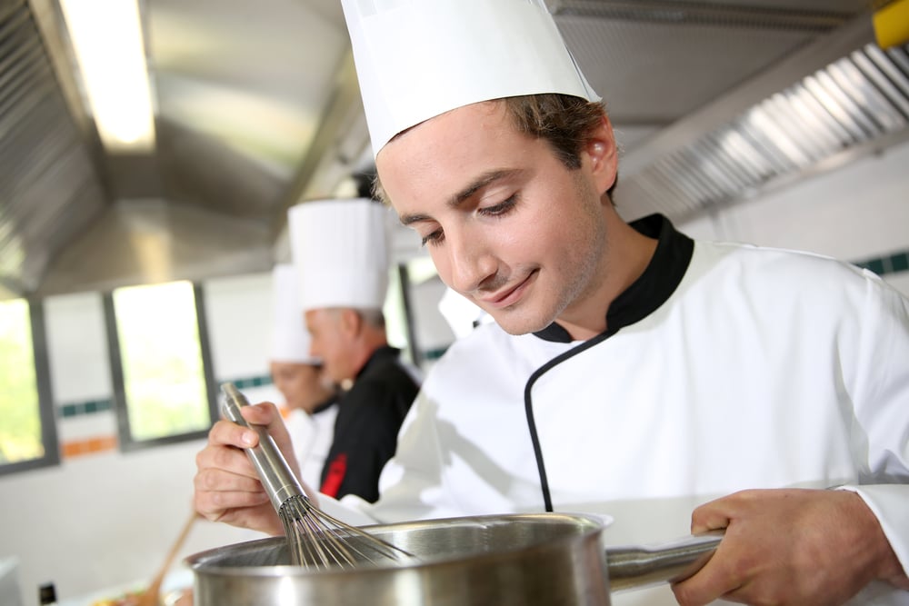 Young cook in restaurant kitchen preparing sauce