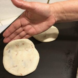 Hand placing a filled pupusa onto a grill