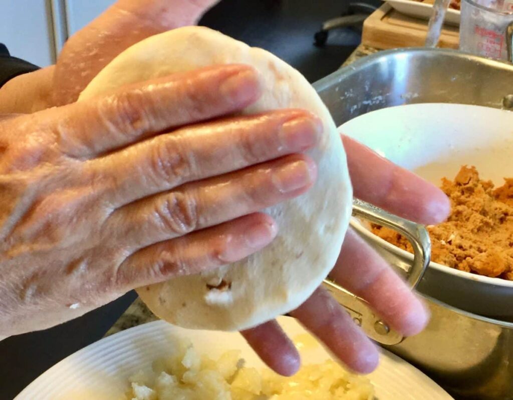 Hand sealing and flattening a pupusa before grilling