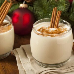 Two glasses of Ron Ponche Panamanian eggnog with cinnamon sticks.