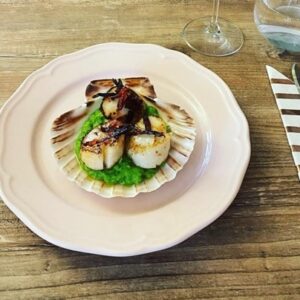 A plated dish of scallops paired with crispy chorizo, set beside a striped napkin.