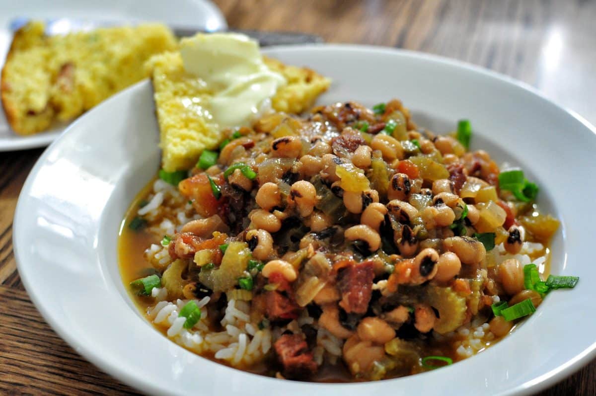 A dish of black-eyed peas served over rice with a side of cornbread.