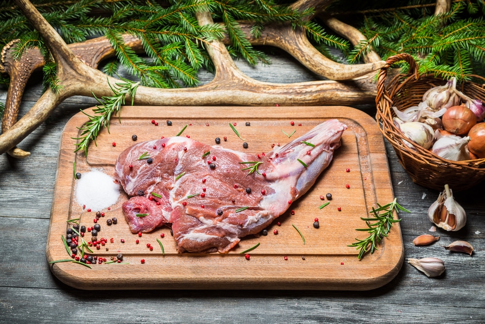 Cut of venison on a cutting board surrounded by garlic, pine boughs and antlers